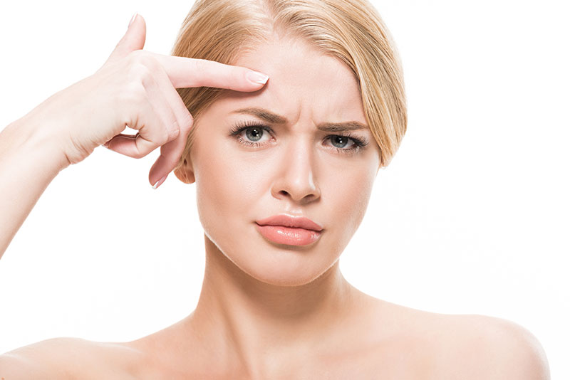 unhappy young woman pointing at wrinkles on forehead