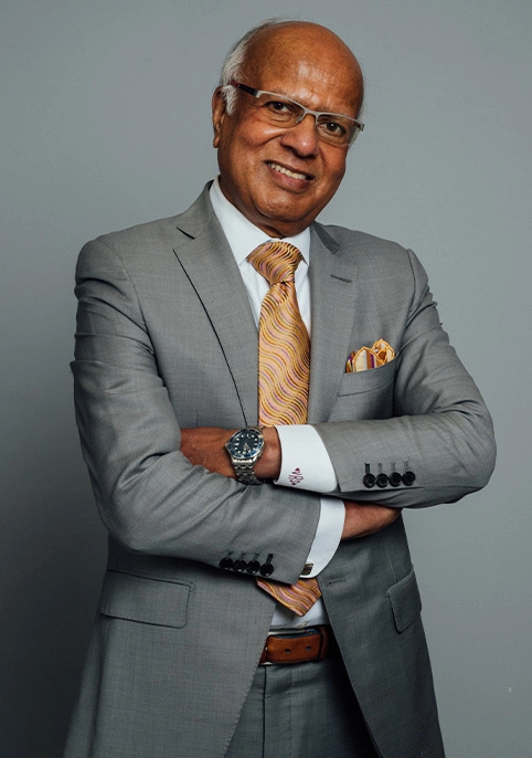 A portrait shot of Dr. Vasdev Rai smiling at the camera in a grey suit, mustard tie and pocket square.