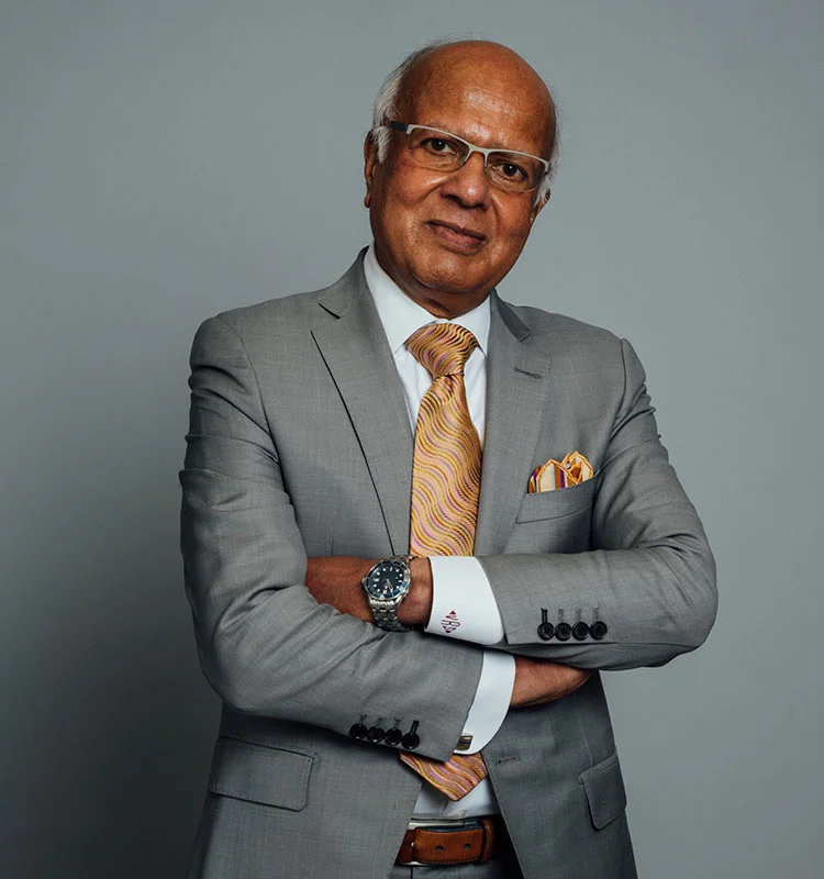 A portfolio shot of Dr. Vasdev Rai wearing a grey suit and mustard multicolored tie, smiling without teeth at the camera. - Doctor in Dallas, TX